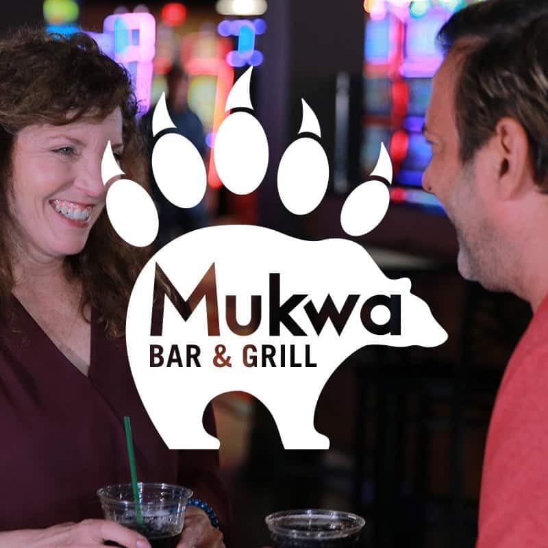 Friendly couple enjoying drinks at Mukwa Bar & Grill, a lively gaming and dining spot at Odawa Casino & Resort.